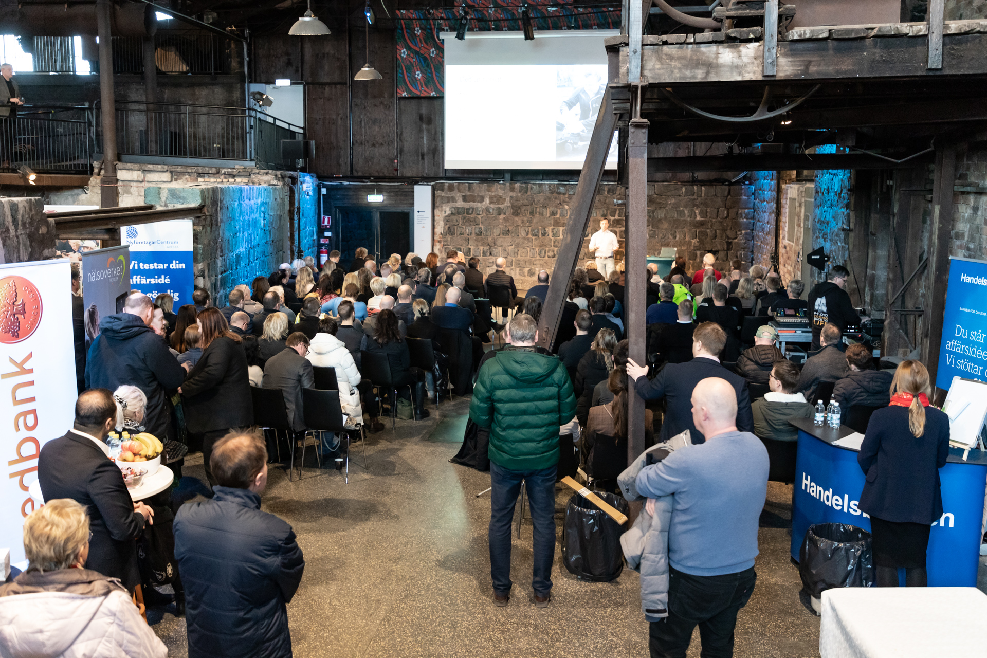 En sittande folksamling lyssnar på en föreläsare.